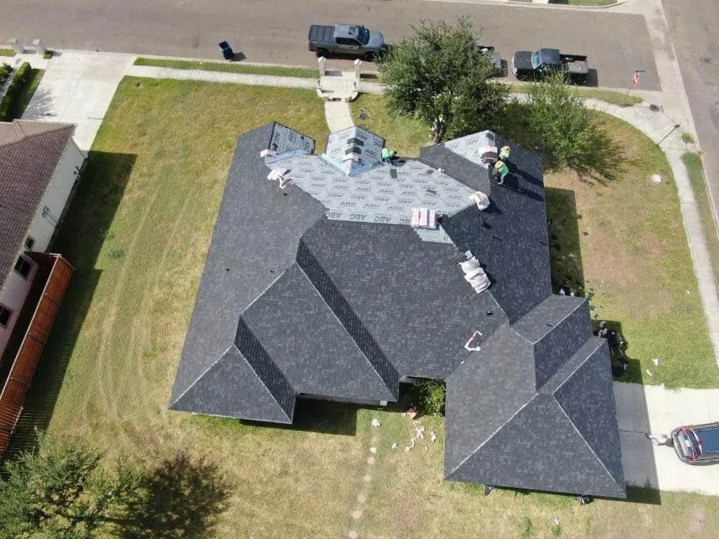 Aerial view of a home with workers applying new roofing shingles in a residential area.