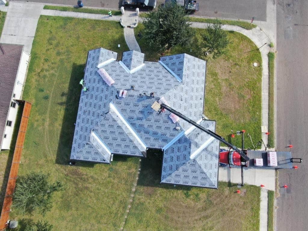 Aerial view of a house under construction with roofing materials and workers on site.